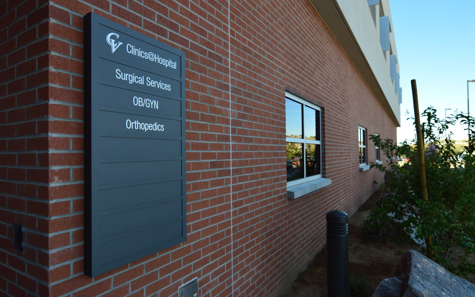 Wall-mounted exterior directory sign identifying hospital clinics, surgical services, OB-GYN and orthopedics