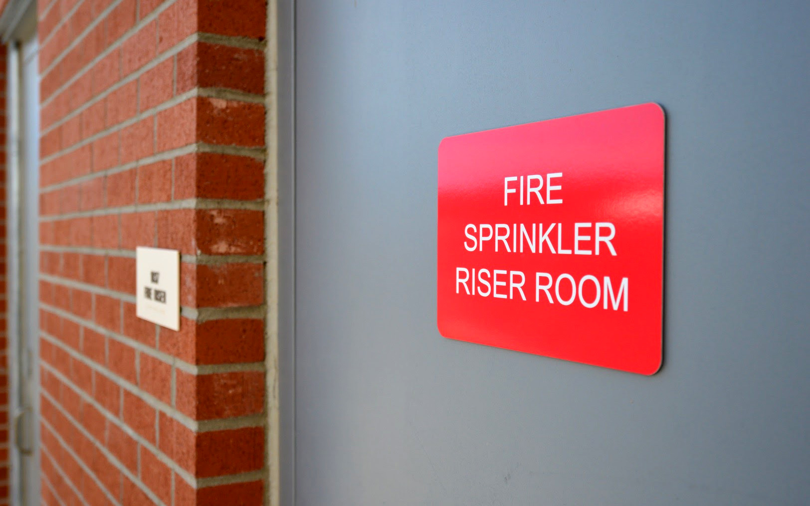 Red exterior panel sign identifying the fire sprinkler riser room at the medical center