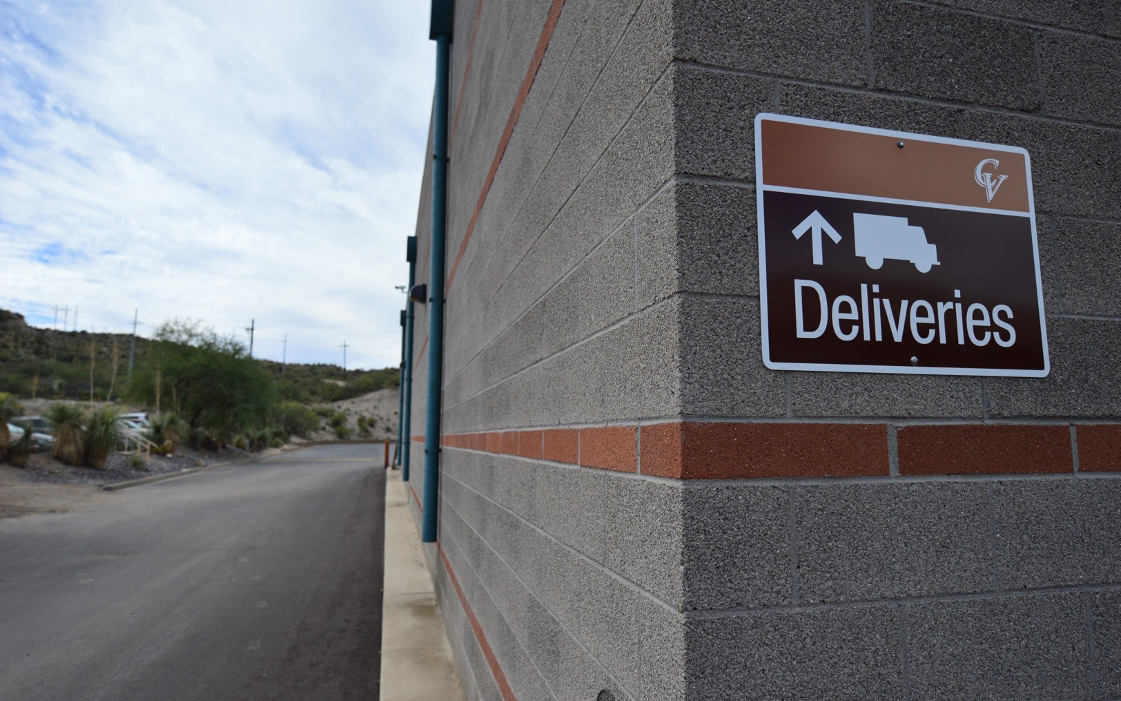 Wall-mounted exterior directional sign with arrow and truck symbol identifying the deliveries route