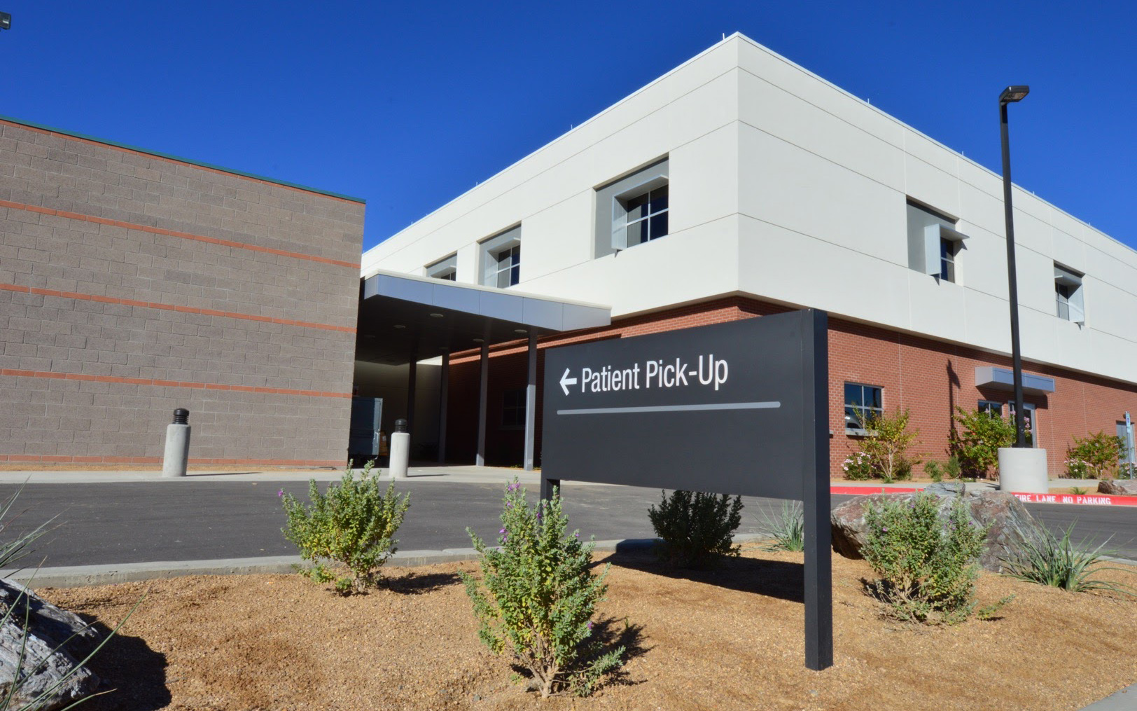 Wide exterior view of a post-and-panel sign directing visitors to patient pick-up