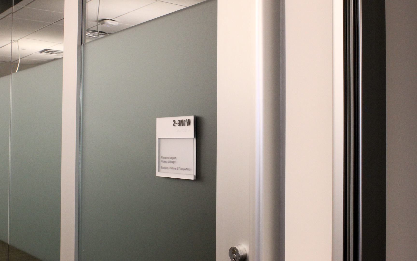 ADA compliant office room sign with flush lens, silver and black finish, custom updatable insert system in corporate interior environment
