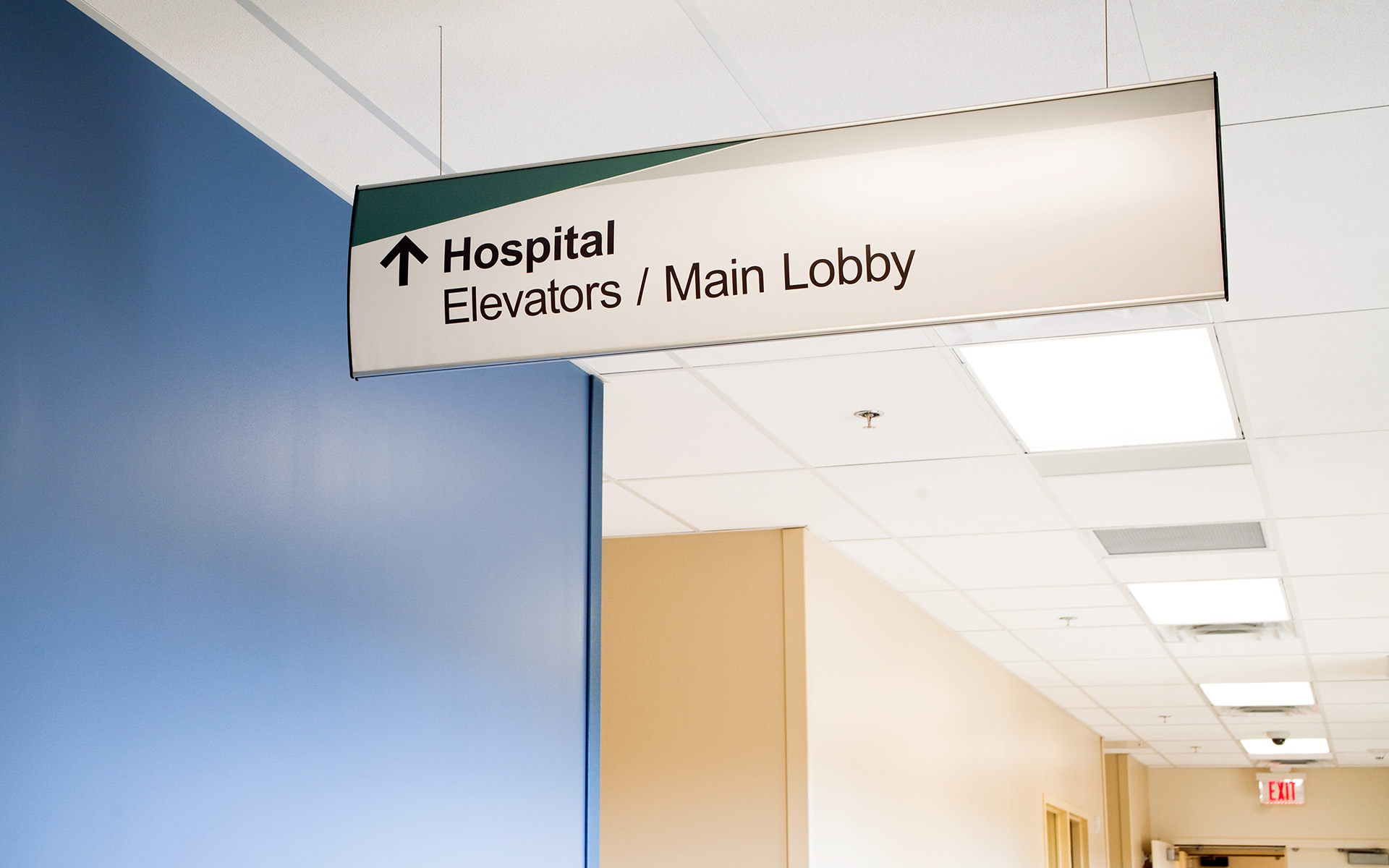 Suspended directional wayfinding sign pointing to hospital elevators and main lobby at UNM Sandoval Regional Medical Center