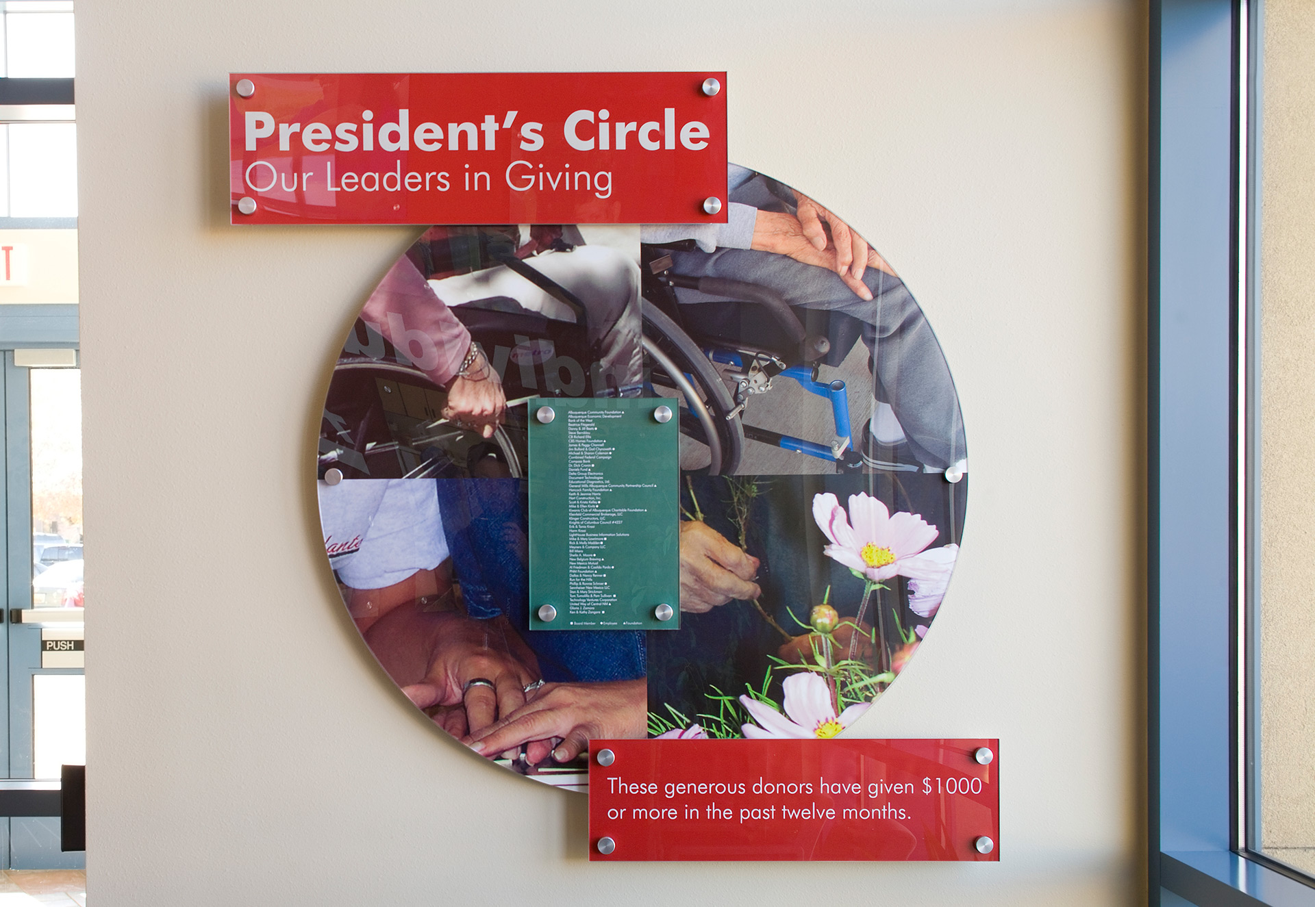 Updateable donor recognition display with clear acrylic panels and anodized standoffs in lobby at Adelante Development Center