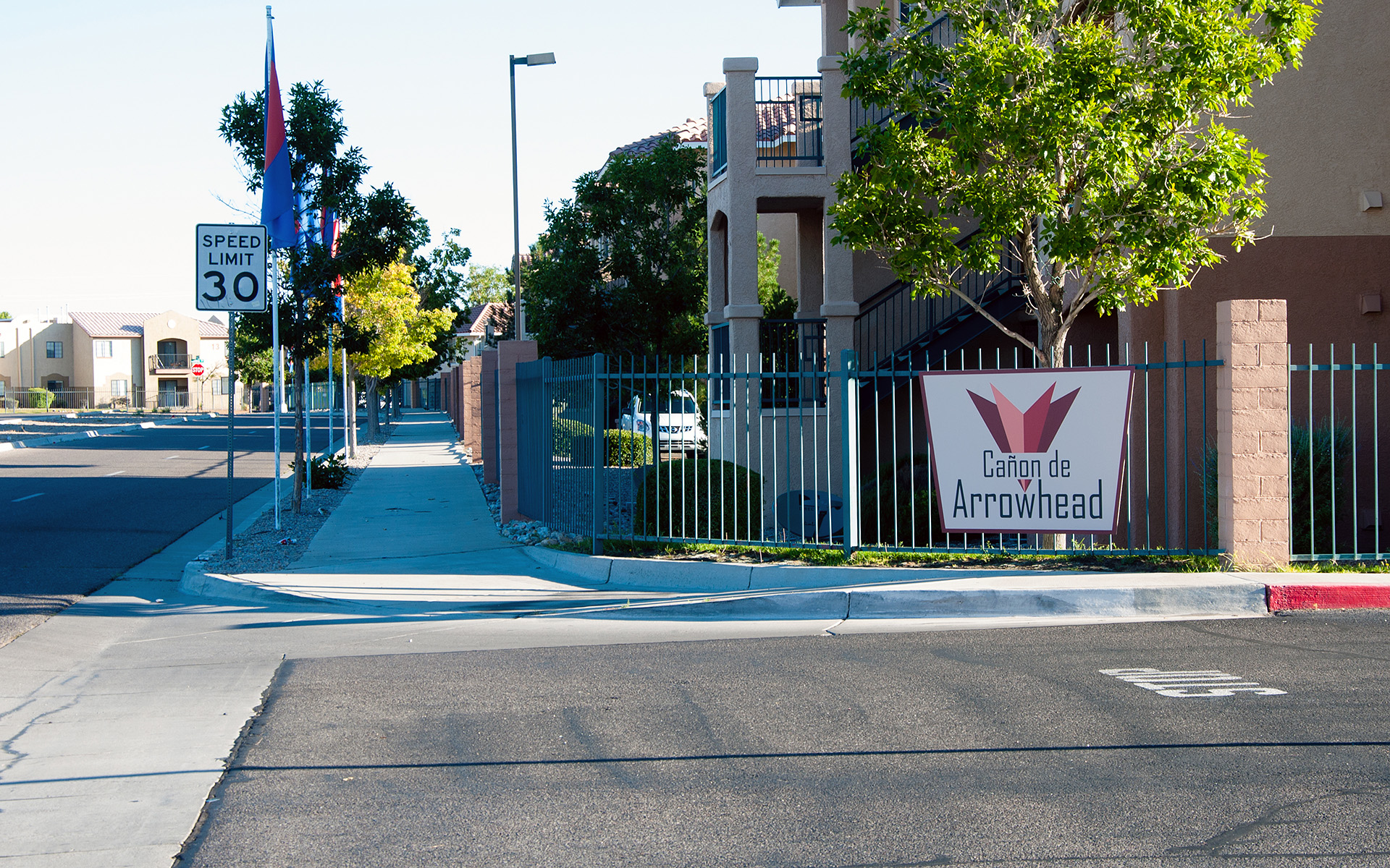 Wide view of apartment community entry signage with streetscape and pedestrian context
