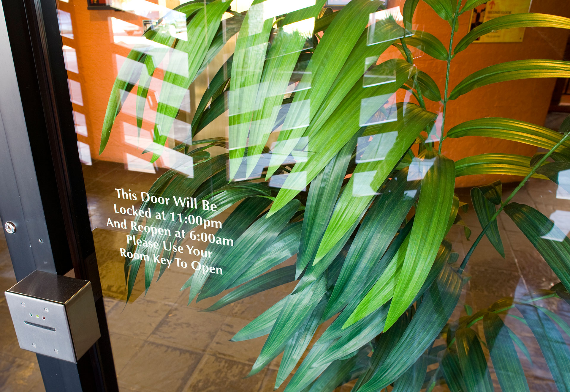 Glass entry door with vinyl lettering showing hours of operation for hotel access