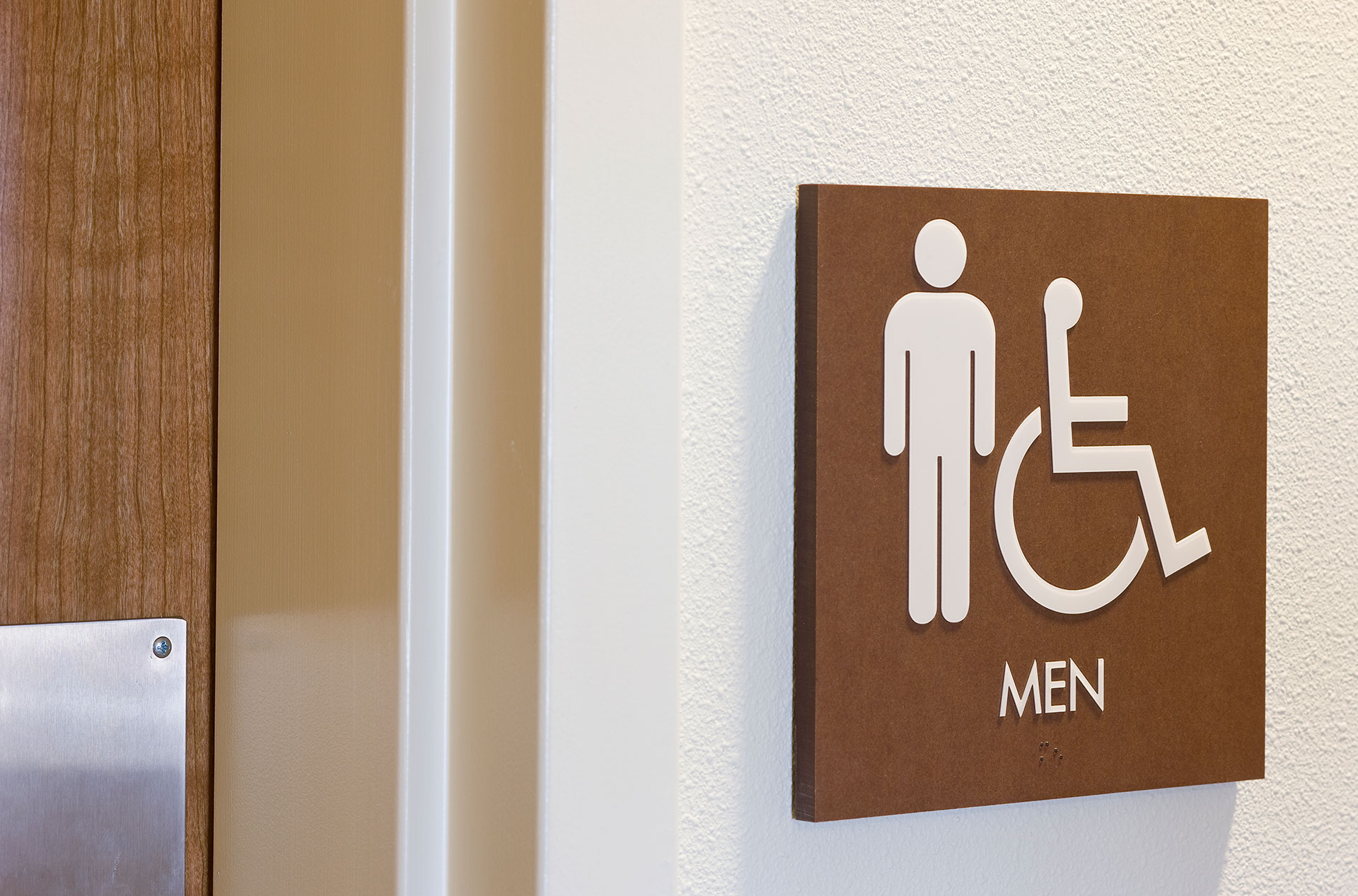 ADA compliant restroom sign with tactile lettering and braille on textured panel