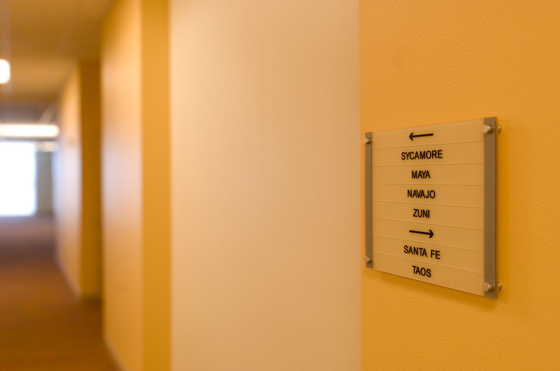 Interior directional wayfinding sign with room names and arrows mounted on wall