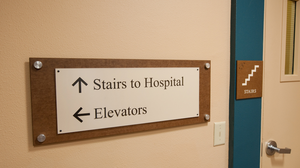Interior hospital directional sign mounted on textured panel with standoff hardware