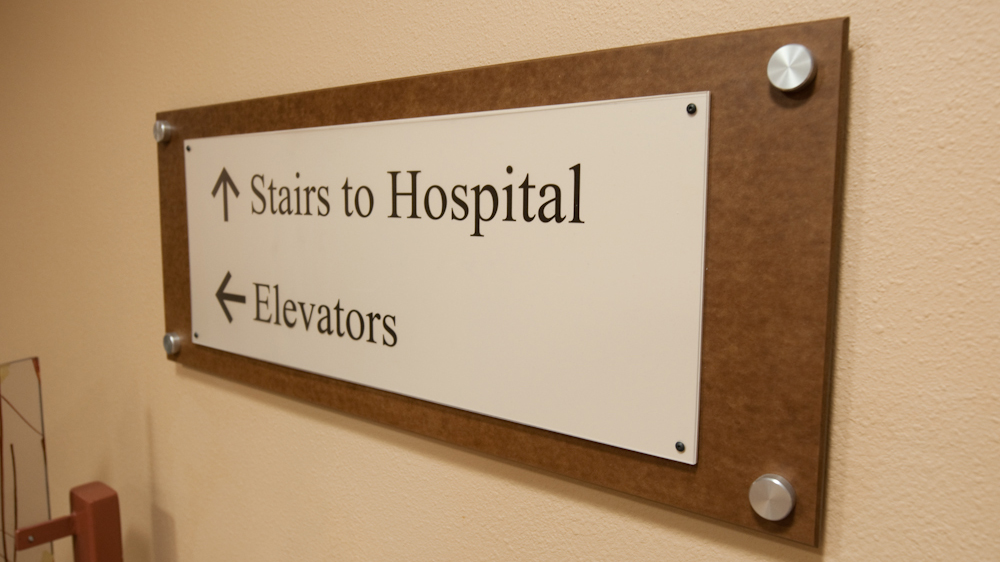 Wall mounted healthcare directional sign with textured frame and standoff hardware