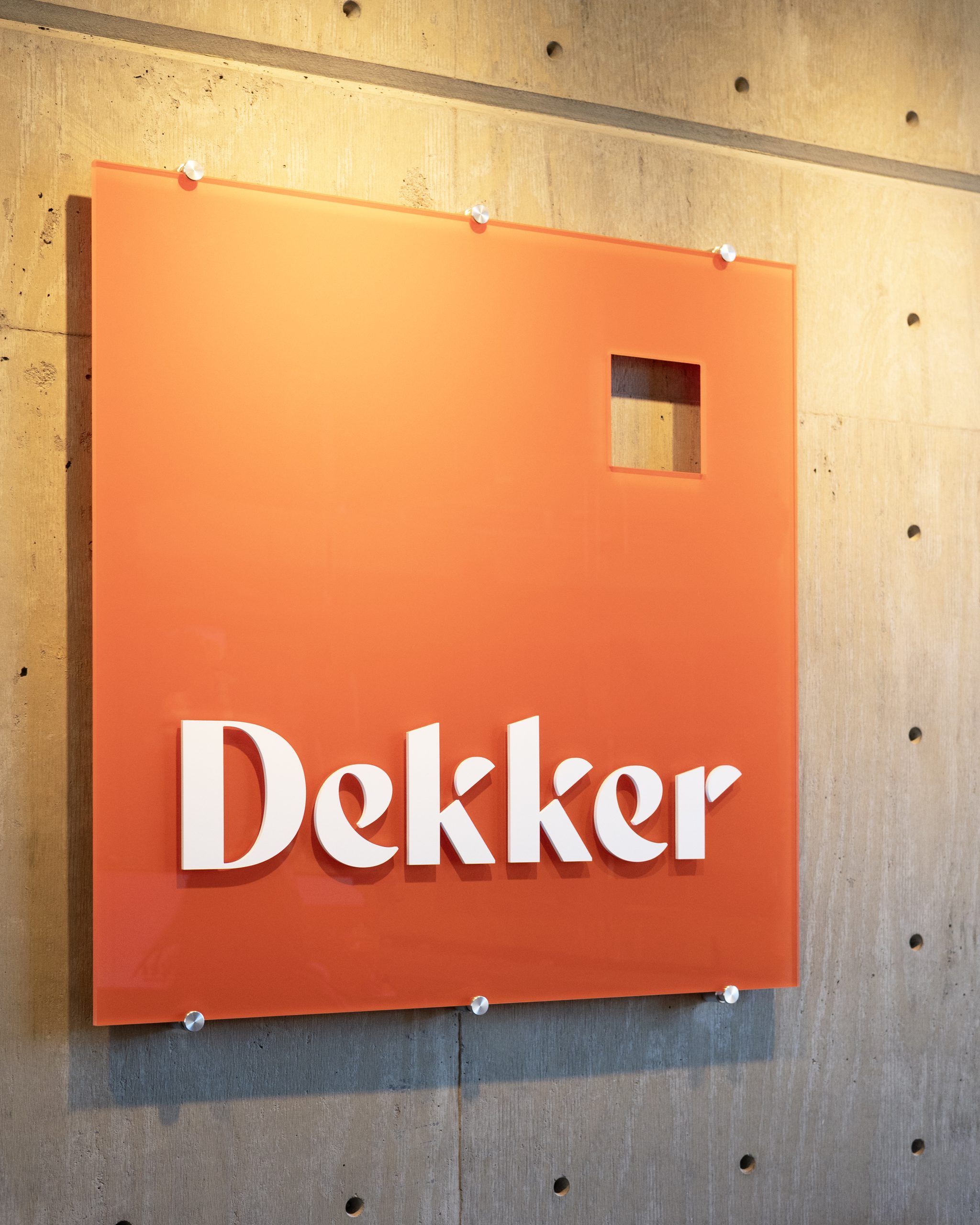 Wide view of Dekker Architects dimensional logo sign installed on exposed architectural concrete wall