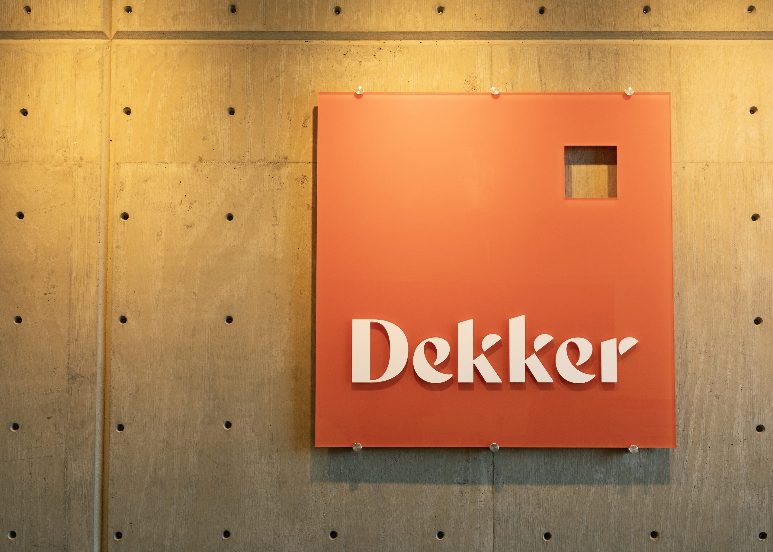 Dekker Architects custom dimensional logo sign with back-painted acrylic panel and flat-cut acrylic letters mounted to exposed concrete wall