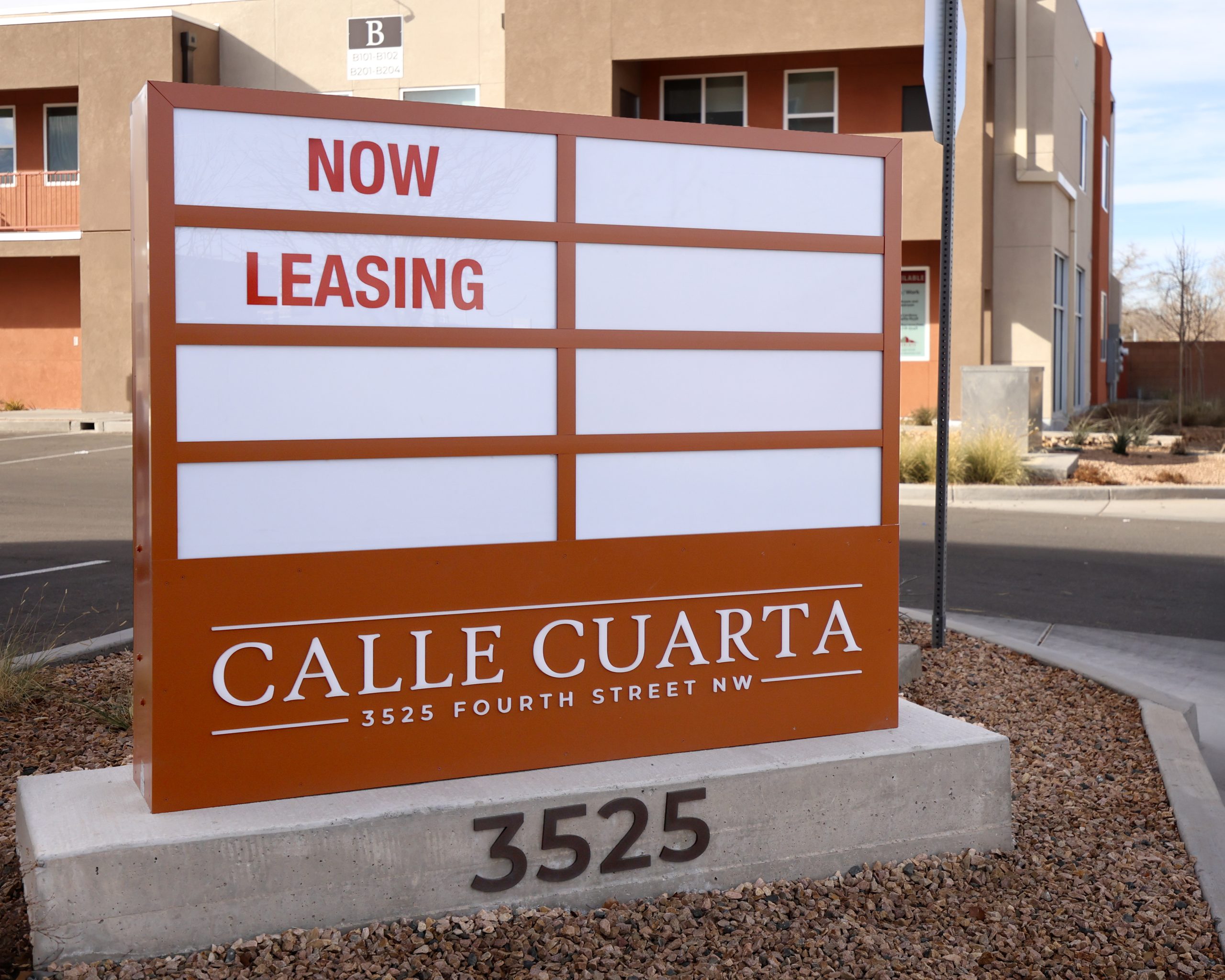 Illuminated monument sign with leasing panels and dimensional address numbers at Calle Cuarta Apartments in Albuquerque.