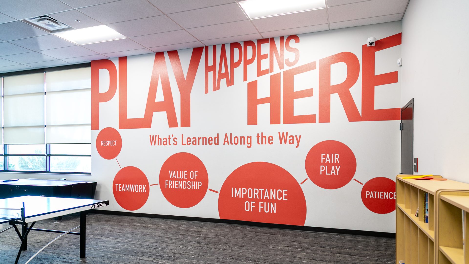 Large orange Play Happens Here wall graphics in a community center recreation room